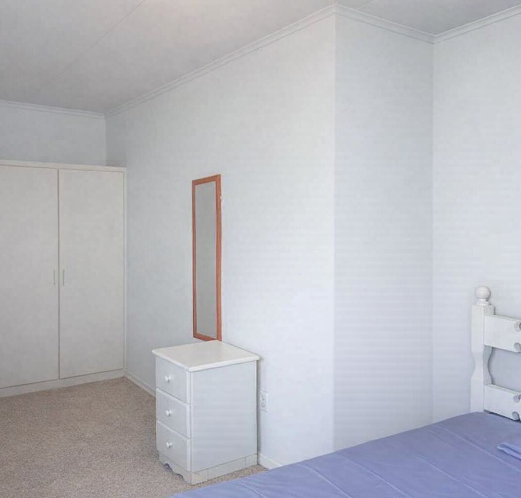 A bedroom with a bed, a dresser, a wardrobe, and a mirror.