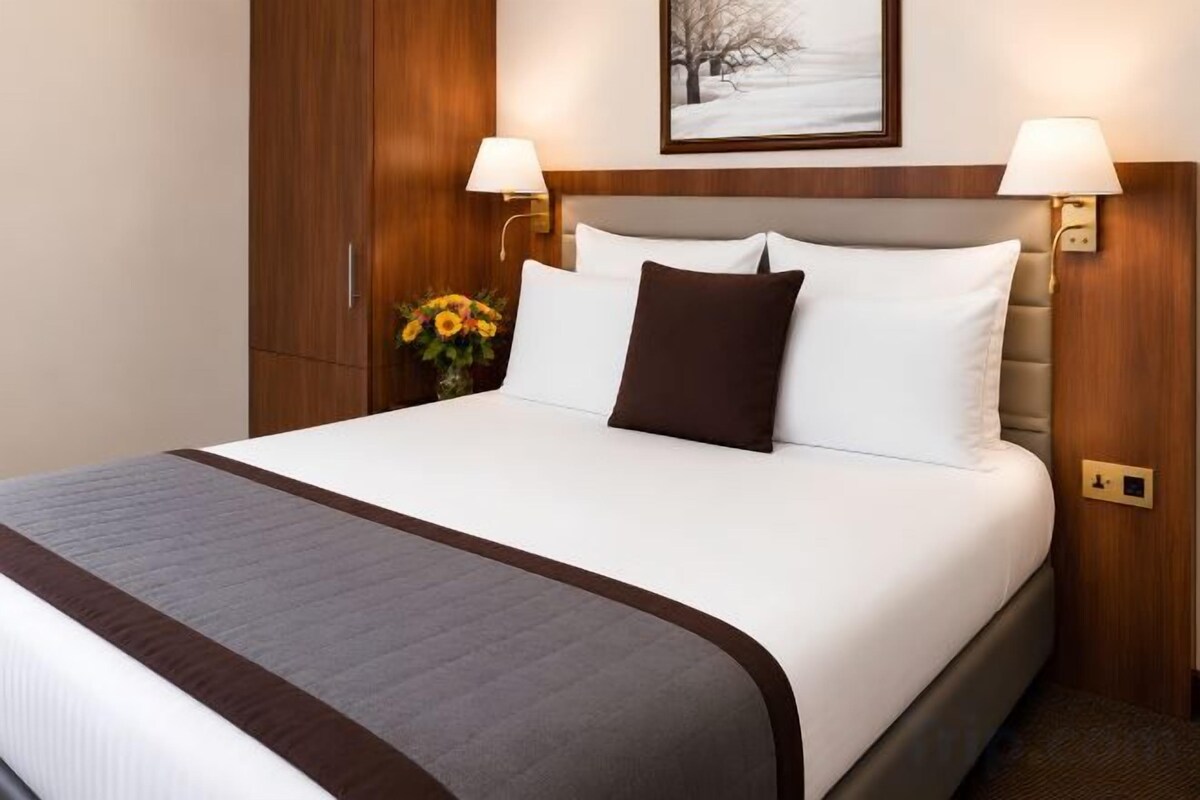 A neatly made bed with a white and brown bedspread, two bedside lamps, and a framed picture above the bed.