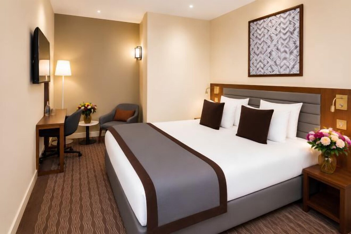 Een hotelkamer met een groot bed, nachtkastjes, een bureau, een stoel, een lamp en een televisie aan de muur.