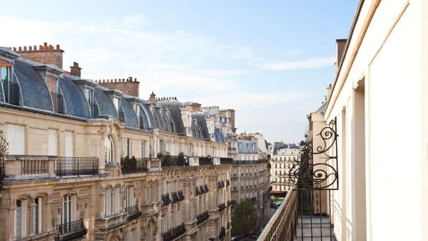 A row of historic buildings with classic architecture, a balcony with wrought iron railings, and a clear sky. - Mayflower Opéra  (Paris)