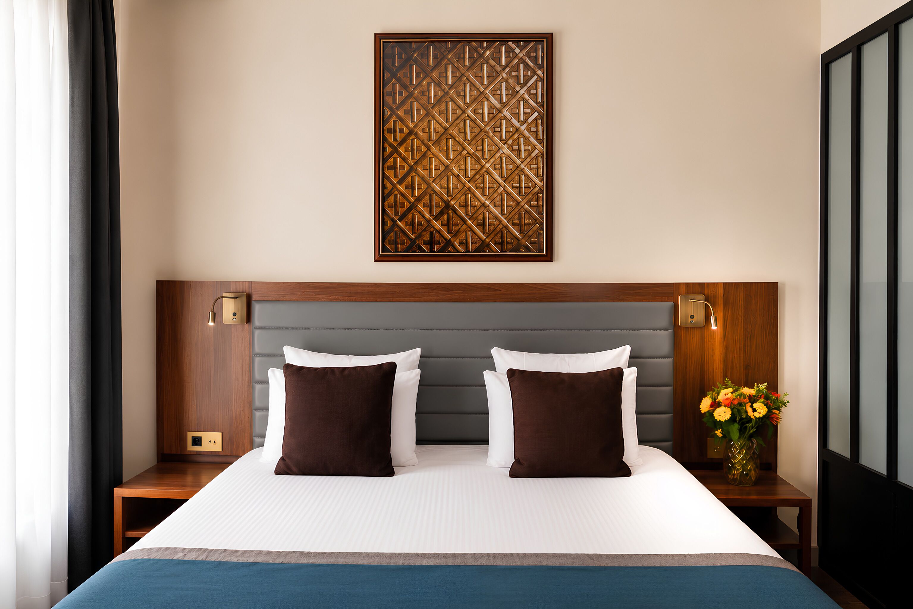 Una habitación de hotel con una cama grande, dos mesitas de noche, una obra de arte en la pared y un florero con flores.