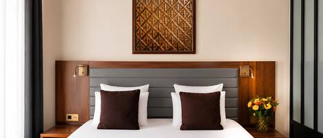 Una habitación de hotel con una cama grande, dos mesitas de noche, una obra de arte en la pared y un florero con flores.