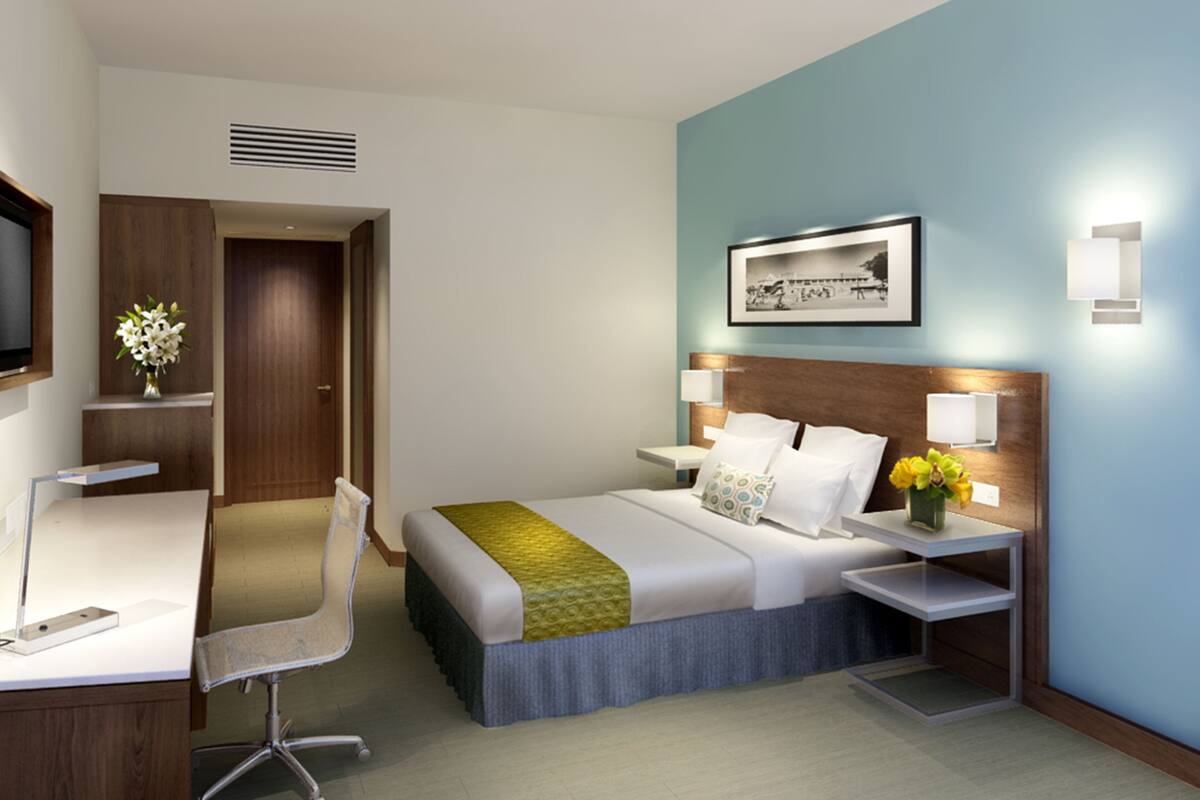 Habitación de hotel con cama, mesitas de noche, escritorio, silla, televisor y un cuadro en la pared.