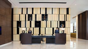 Een receptiezone met een modern design, met een receptiebalie, twee medewerkers en een decoratieve wand met verticale panelen.