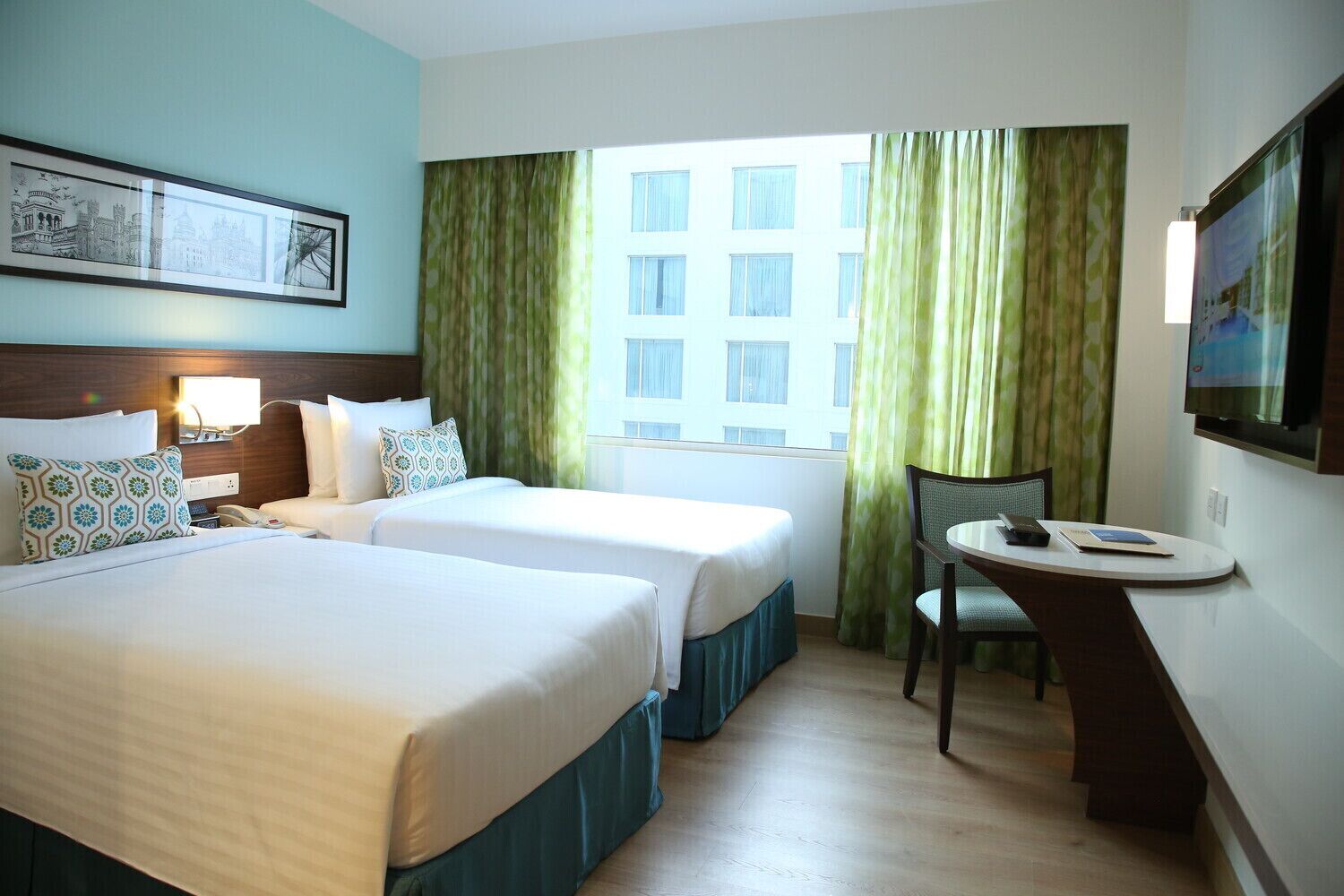 A hotel room with two beds, a desk, a chair, a TV, and a window with curtains.