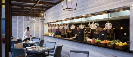 A restaurant with a long counter, multiple hanging light fixtures, and a chef preparing food.