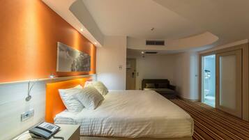 A hotel room with a bed, a bedside telephone, and a view of the bathroom through a glass door.