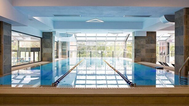 Una piscina interior con paredes de vidrio transparente, un diseño de techo moderno y pilares de piedra.