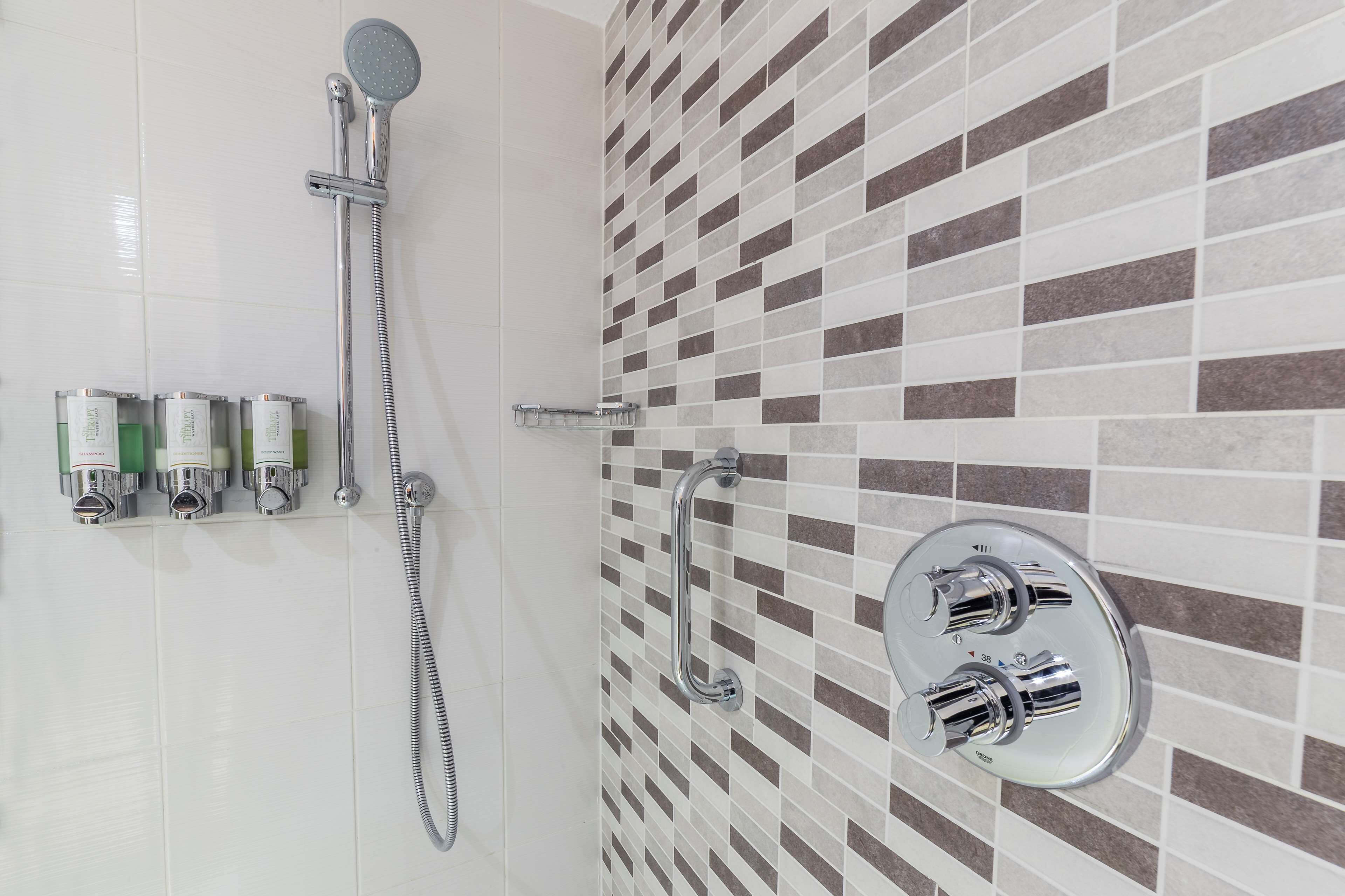 A bathroom with a shower, a handrail, and a wall-mounted faucet.