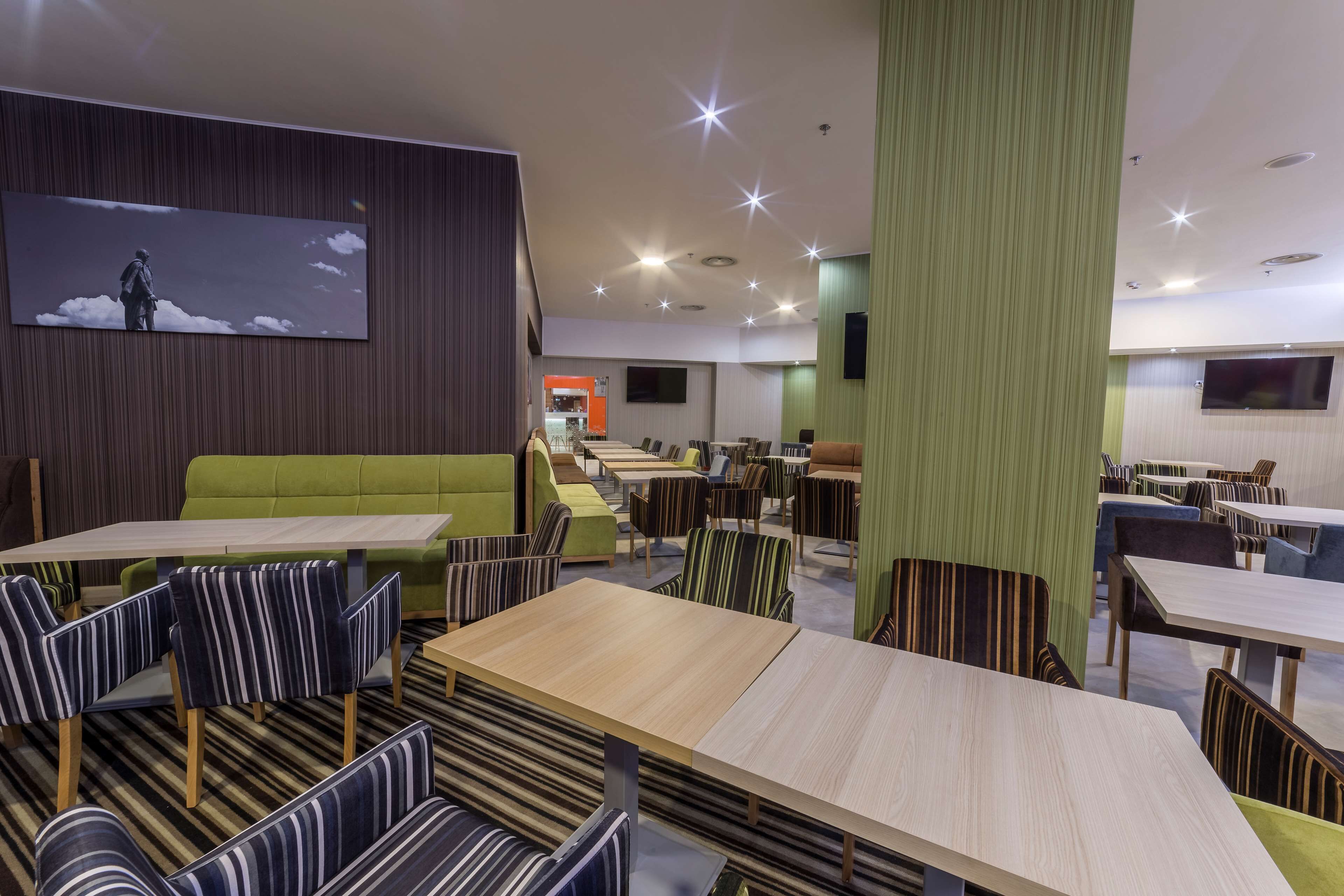 A modern dining area with striped chairs and tables, a green sofa, and a flat-screen TV on the wall.