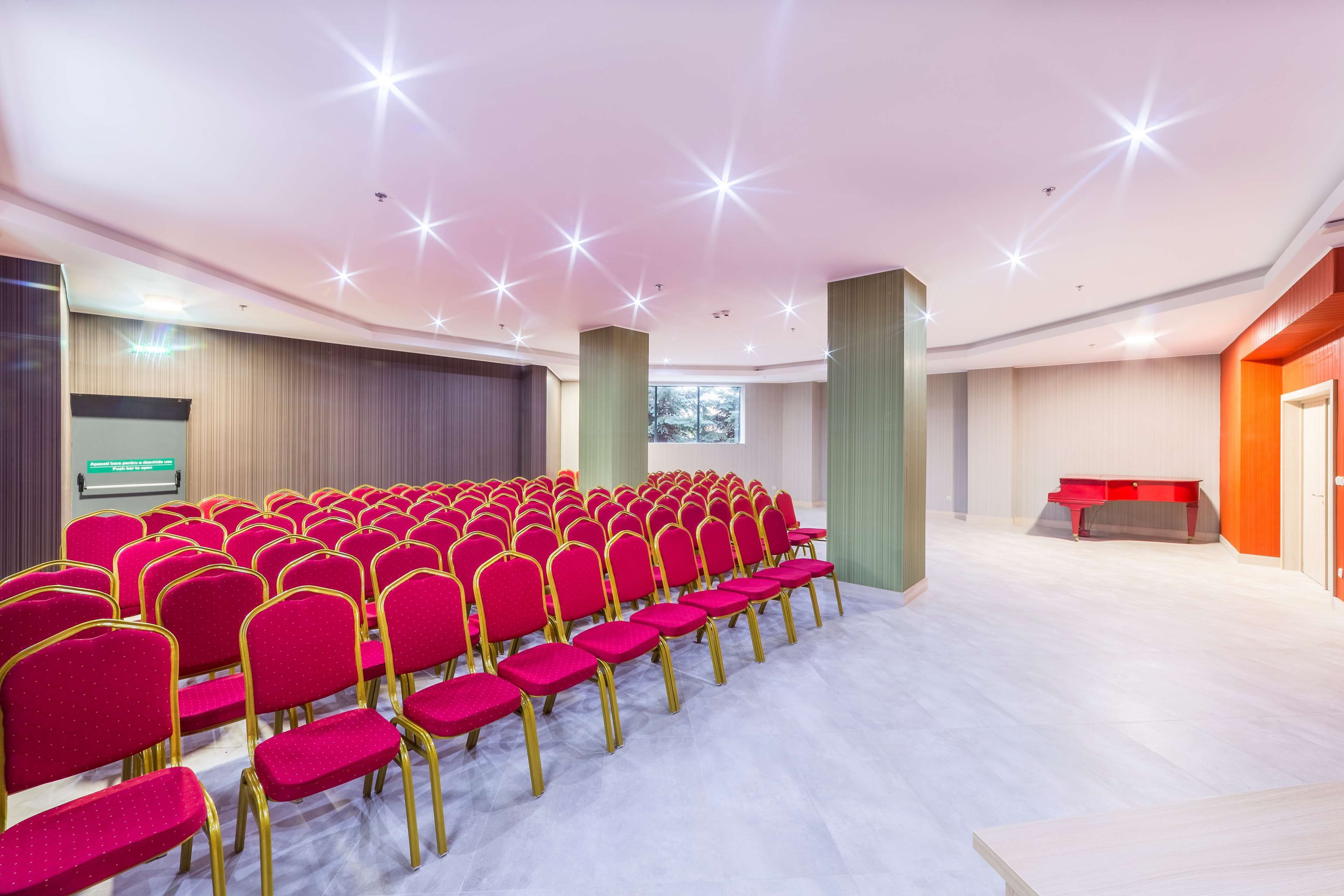 A conference room with rows of red chairs, a projector screen, and a red table.