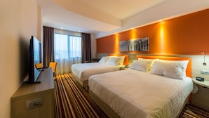 Habitación de hotel con dos camas, televisión, escritorio y ventana con cortinas.