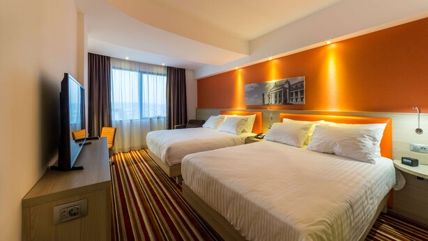 Une chambre d’hôtel avec deux lits, une télévision, un bureau et une fenêtre avec des rideaux.