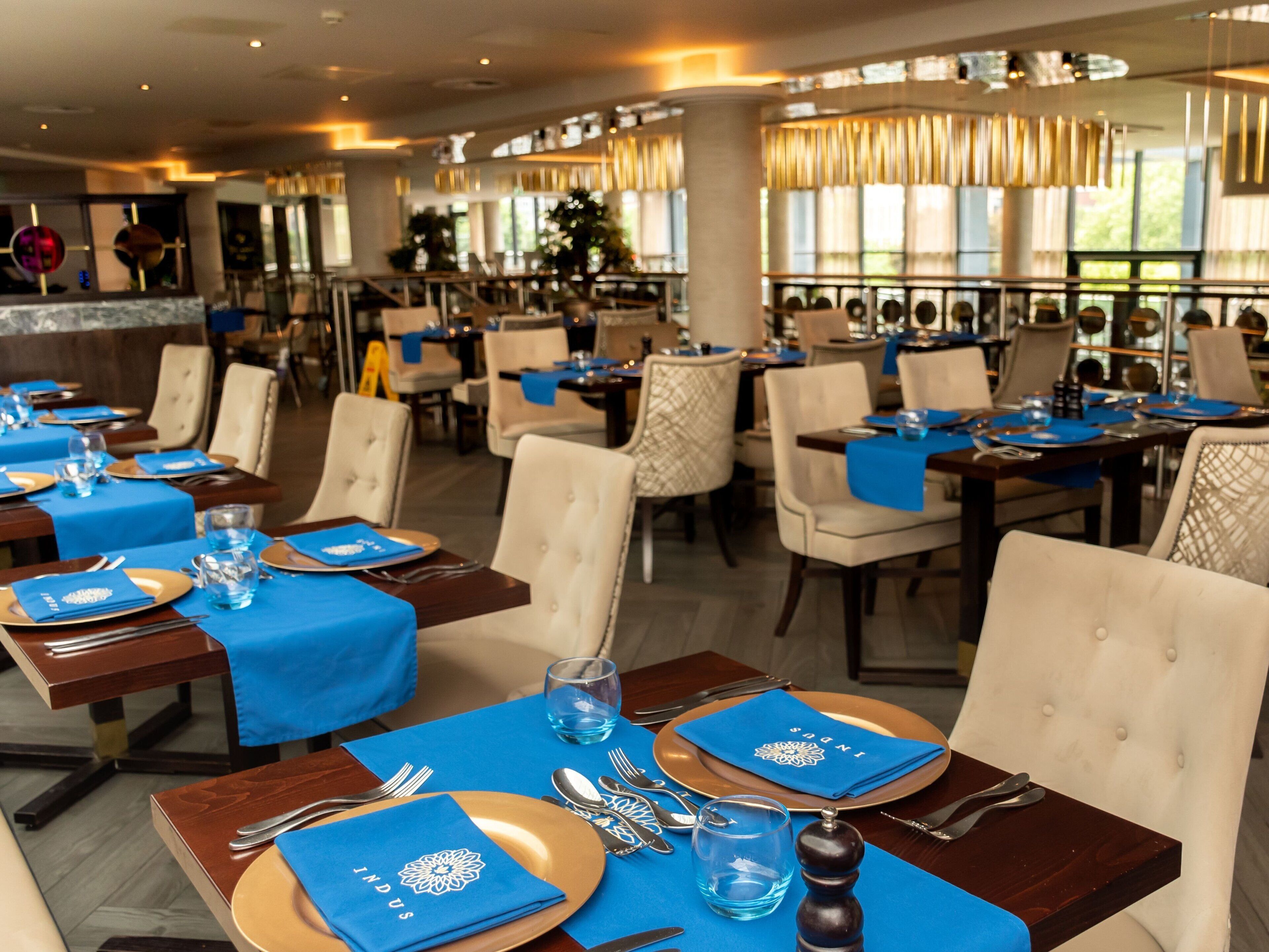 A restaurant with tables set for dining, featuring blue tablecloths and gold plates.