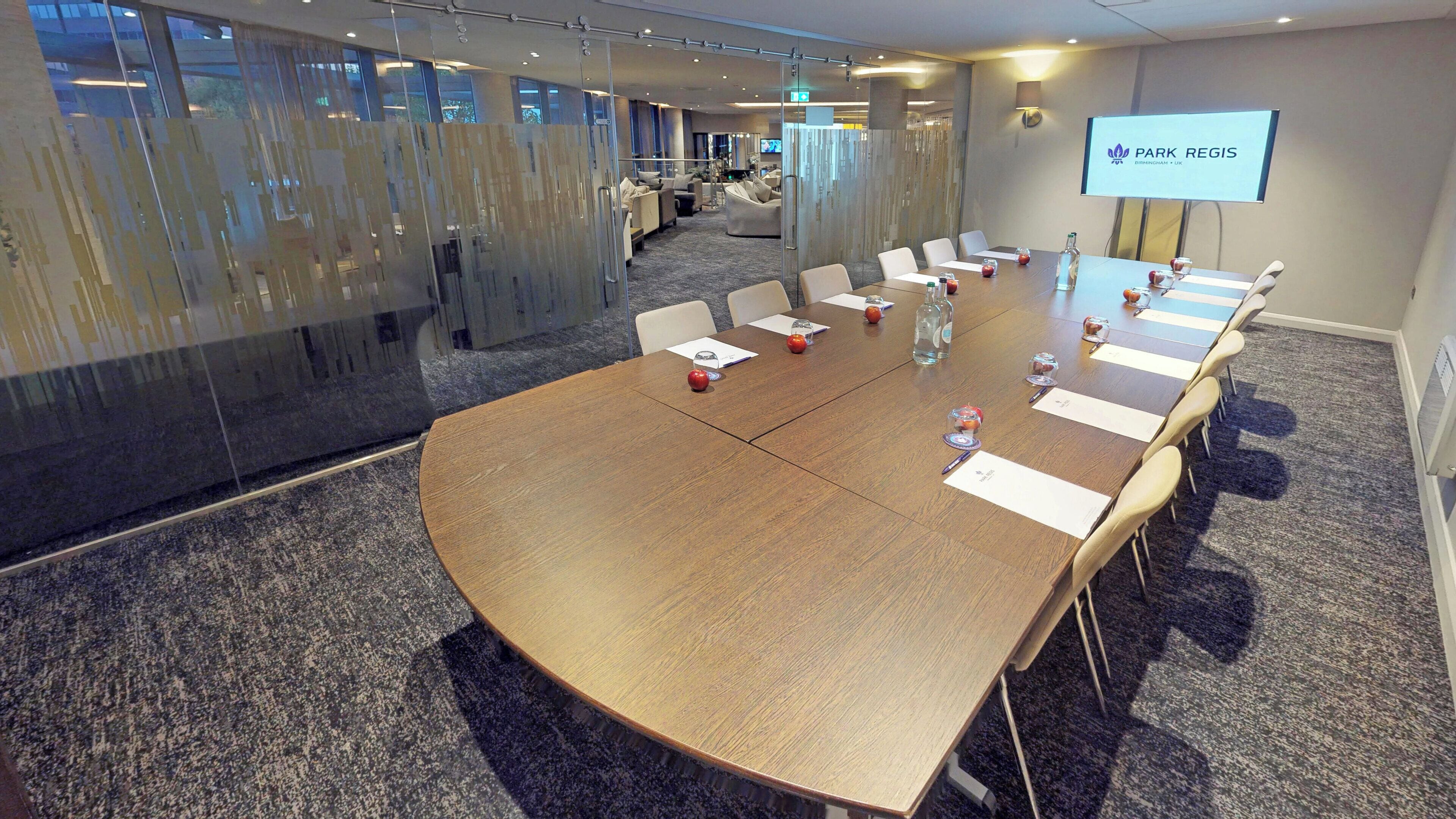 A conference room with a large oval table, glass partitions, and a projection screen displaying 'Park Regis'.