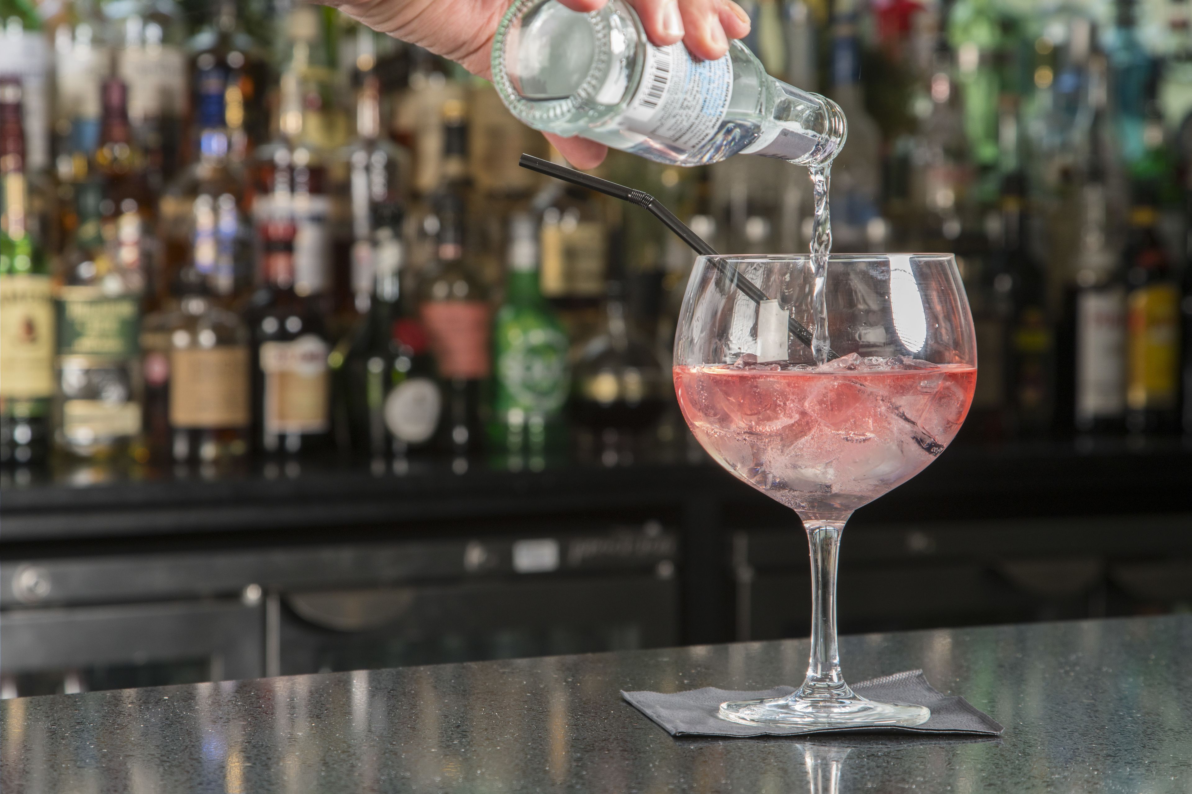 A bartender pouring a drink into a glass with a straw.