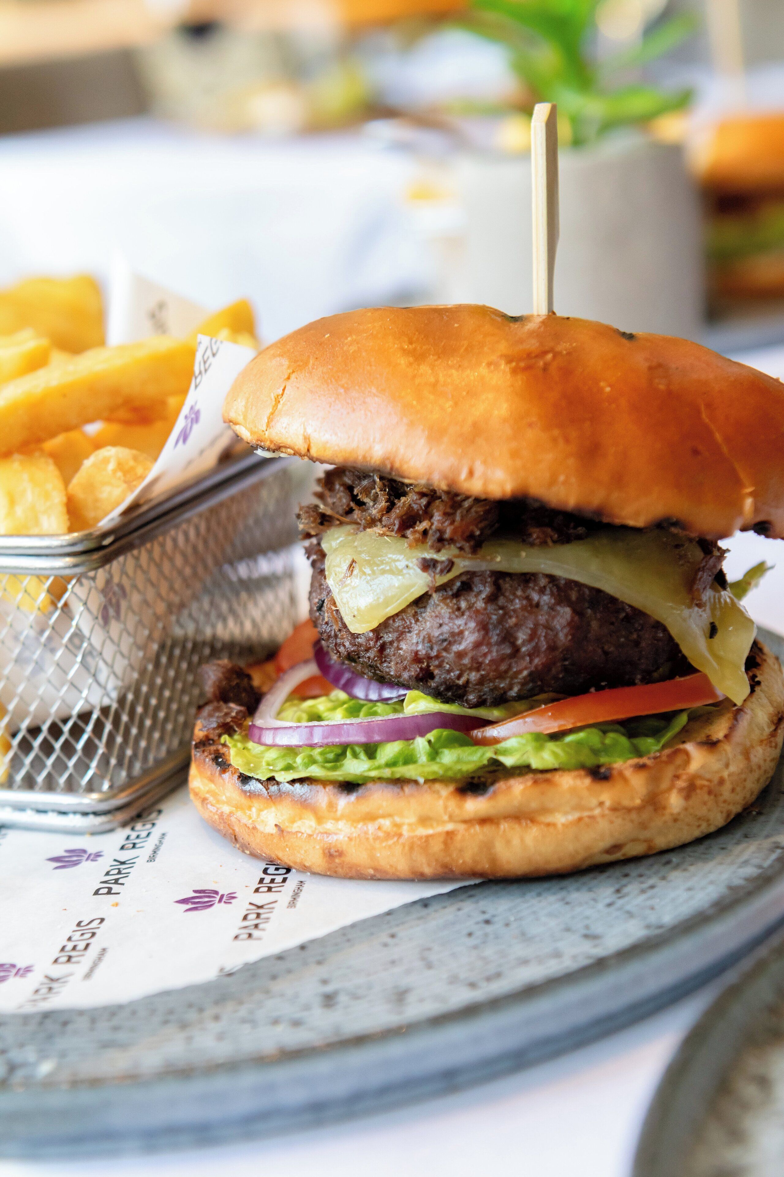 Una hamburguesa con pan, lechuga, tomate, cebolla y queso, acompañada de una cesta de papas fritas.