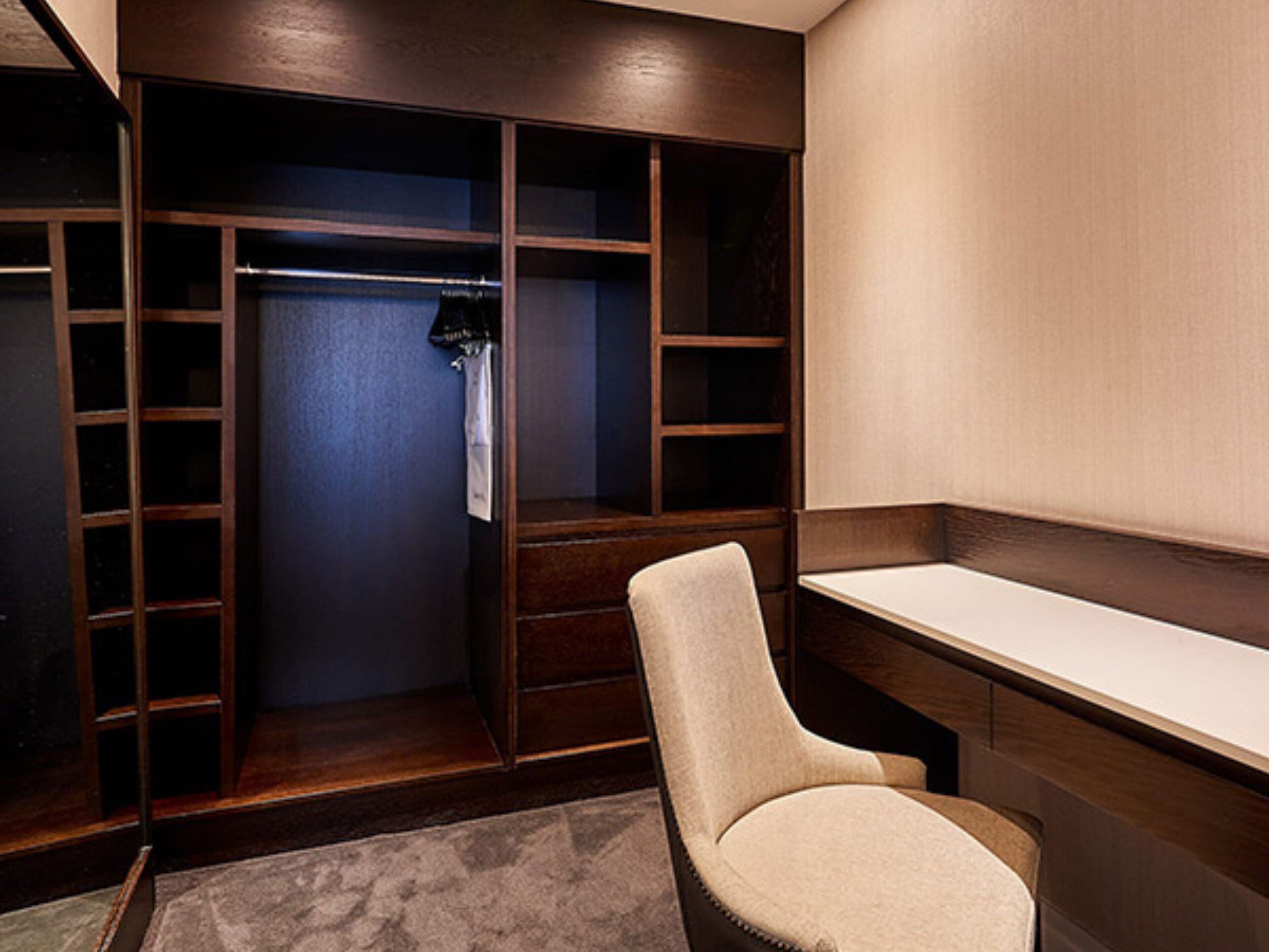A walk-in closet with wooden shelving, a chair, and a mirror.