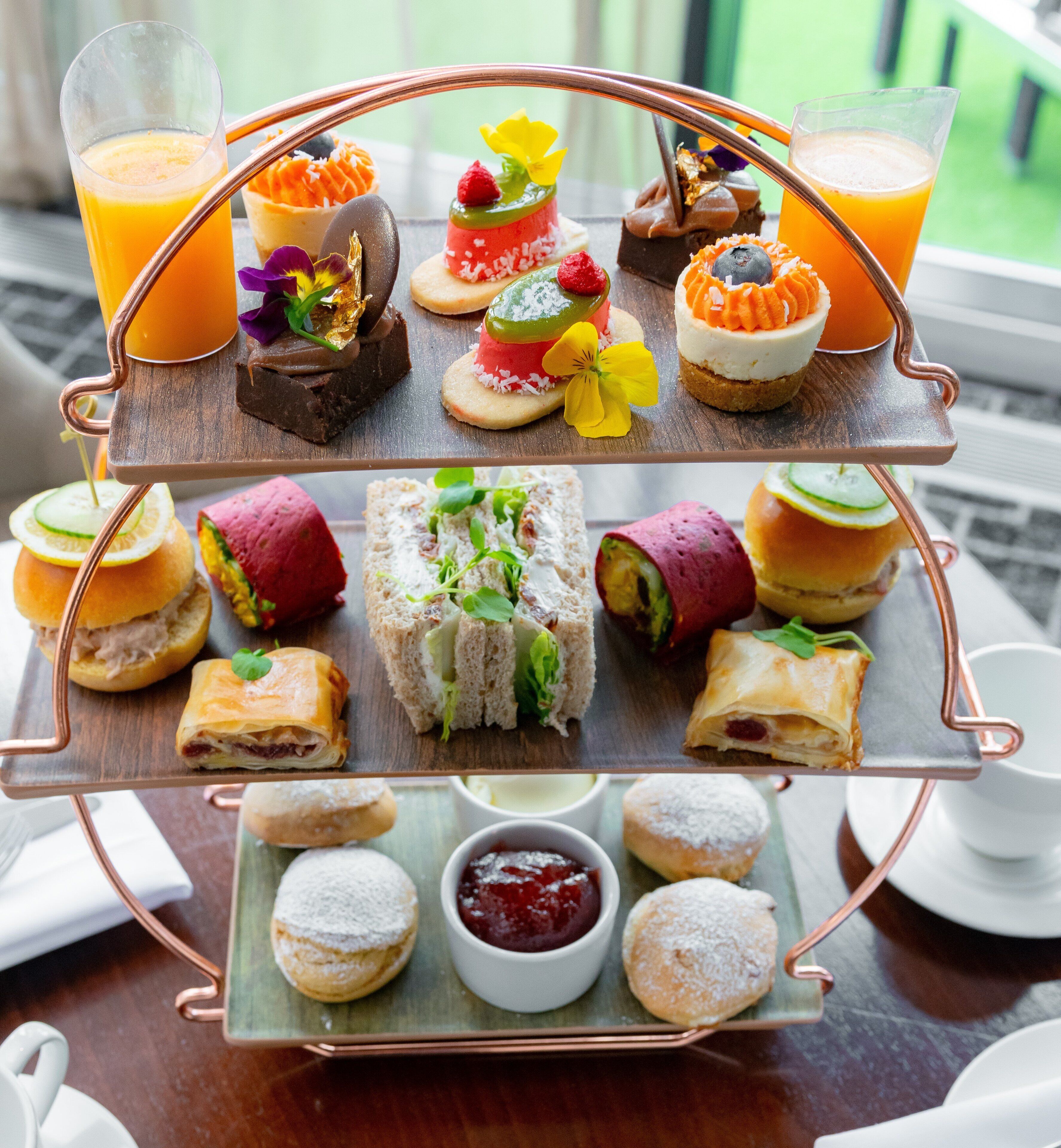 A two-tiered tray with various pastries, sandwiches, and drinks, likely a dessert or snack selection.