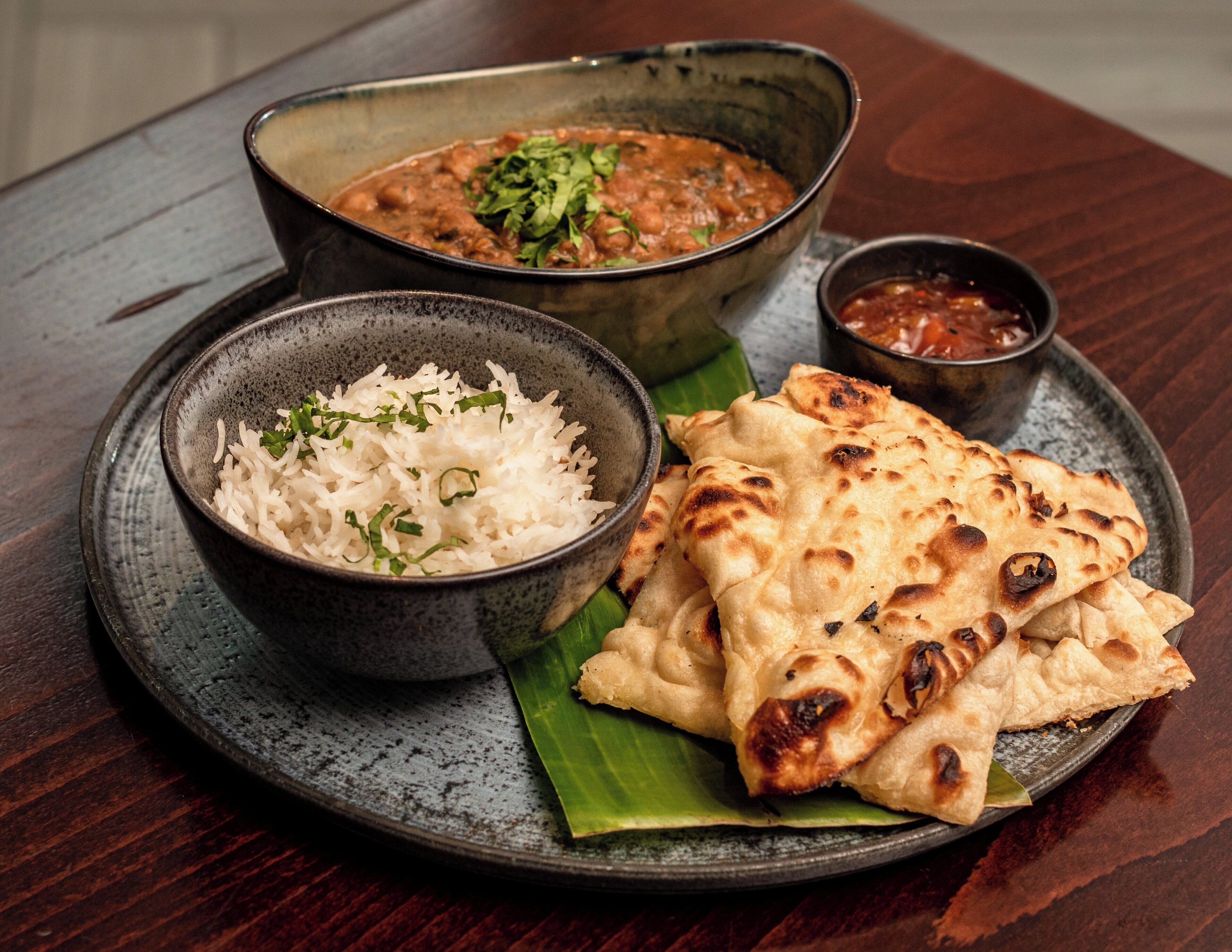 A plate with rice, naan bread, and a bowl of curry on a wooden table.