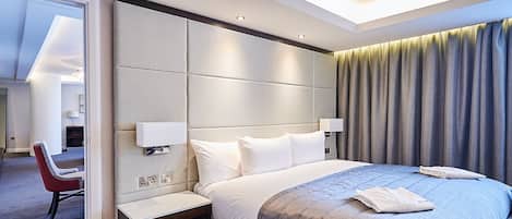 A modern hotel room with a large bed, a bedside table, a nightstand, and a view of the hallway.