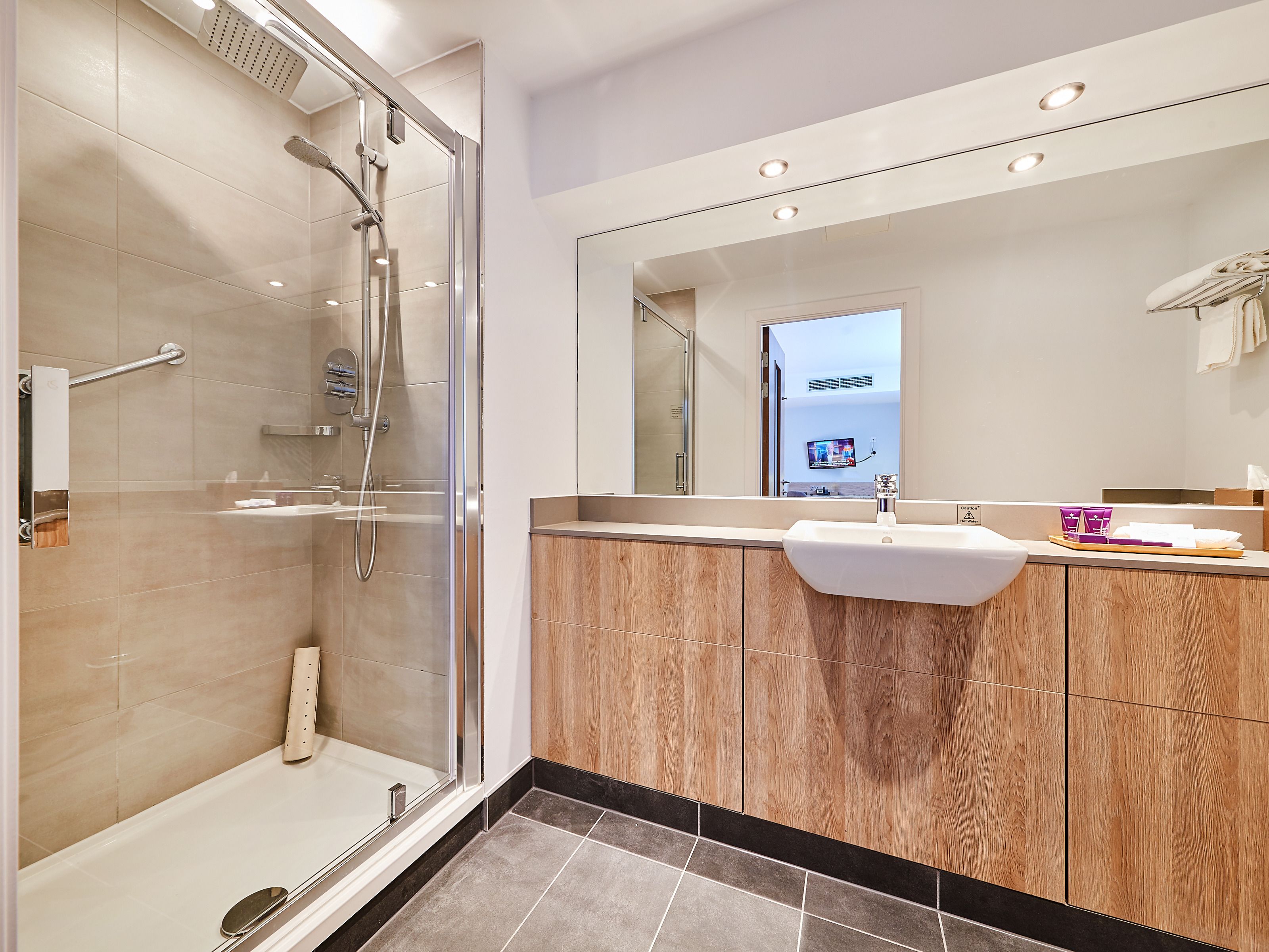 A modern bathroom with a glass-enclosed shower, a vanity with a sink, and a large mirror.