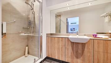 A modern bathroom with a glass-enclosed shower, a vanity with a sink, and a large mirror.