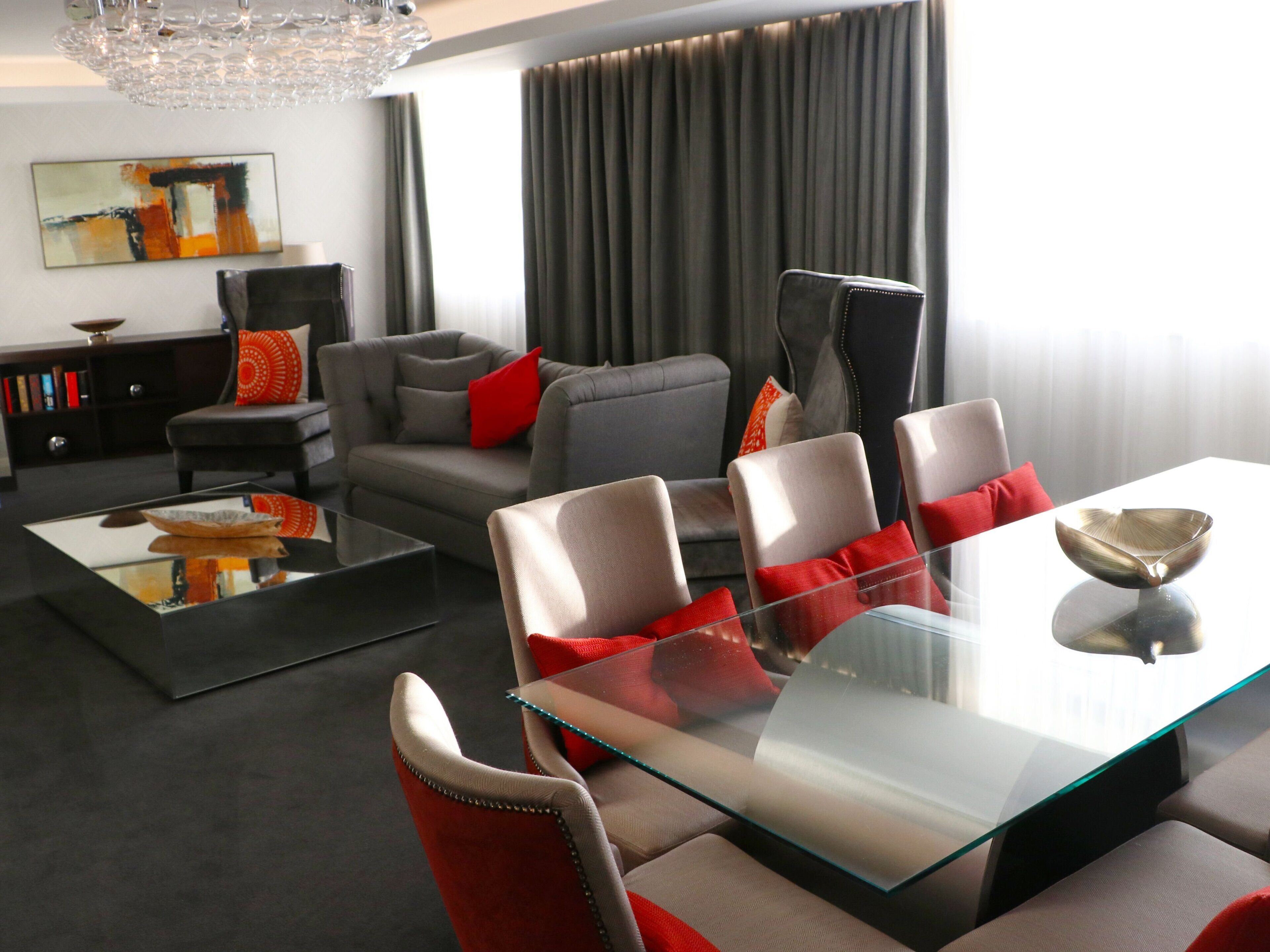 A modern living room with a glass coffee table, grey sofas, and red cushions.