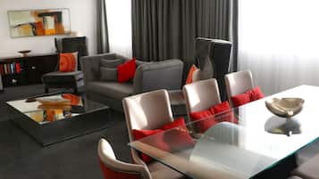 A modern living room with a glass coffee table, grey sofas, and red cushions.