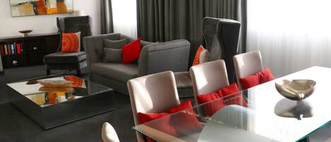 Un salon moderne avec une table basse en verre, des canapés gris et des coussins rouges.