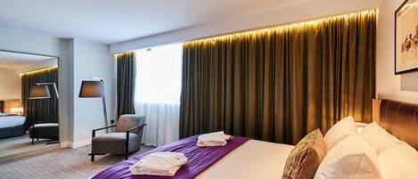 Una habitación de hotel con una cama grande, una silla, un escritorio y una ventana con cortinas.