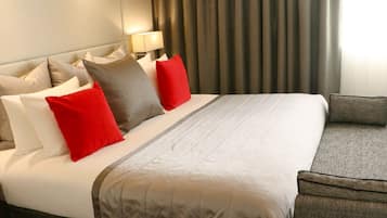 Une chambre d’hôtel avec un grand lit, plusieurs oreillers, une tête de lit, une table de chevet avec une lampe et une vue sur l’extérieur à travers des rideaux.