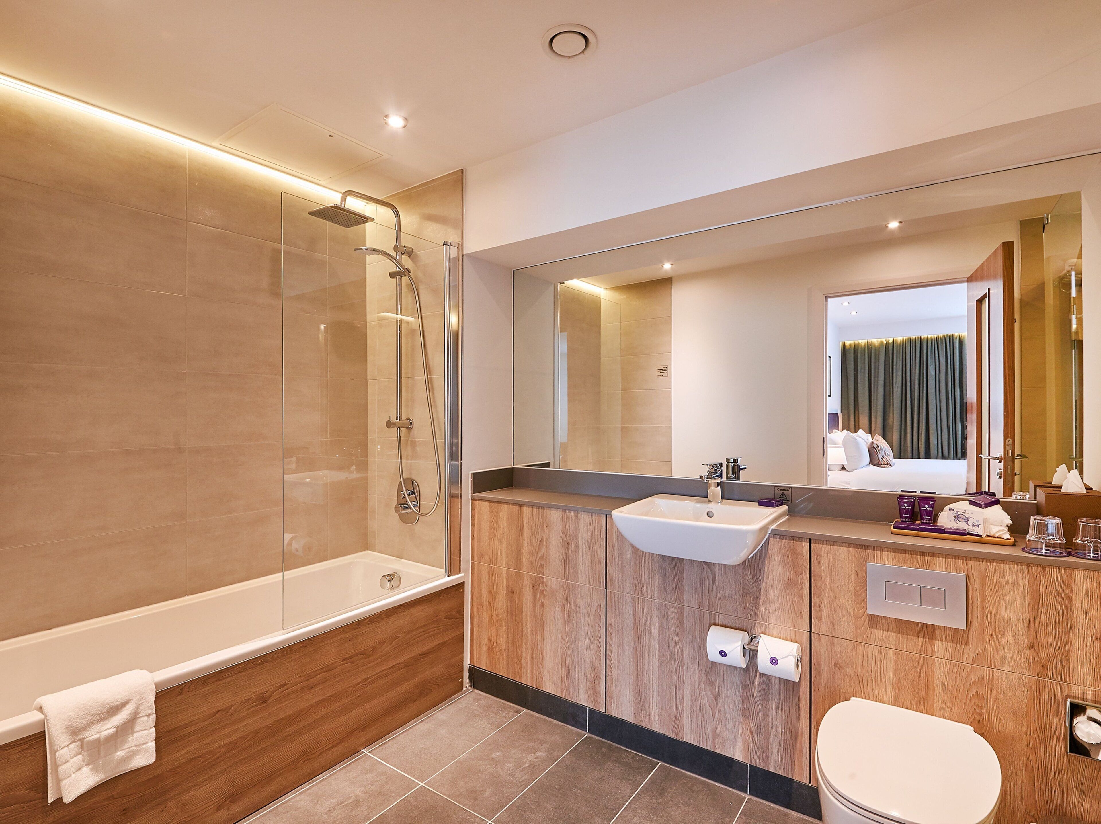 A modern bathroom with a glass-enclosed shower, a wooden vanity, a large mirror, and a visible toilet.