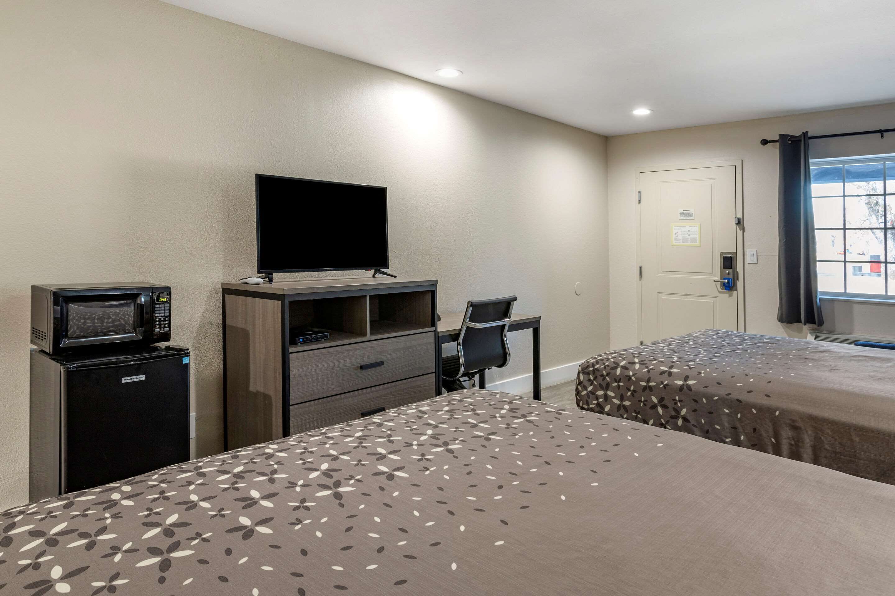 Habitación de hotel con dos camas, un escritorio, una silla, un televisor de pantalla plana, un microondas y una puerta con vista al exterior.