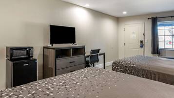 Habitación de hotel con dos camas, un escritorio, una silla, un televisor de pantalla plana, un microondas y una puerta con vista al exterior.