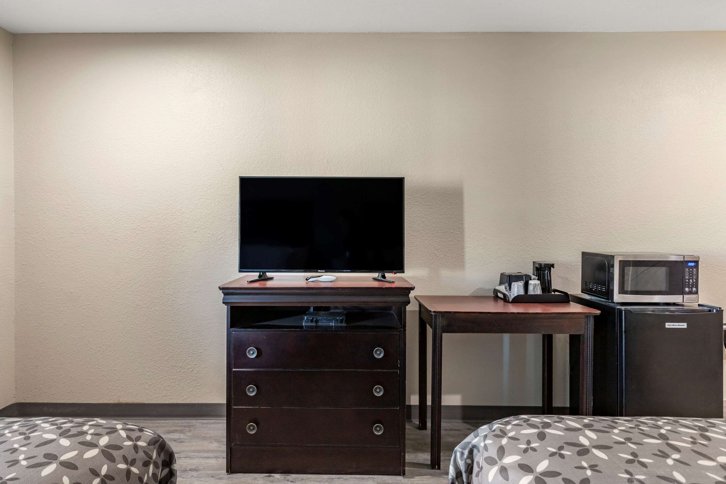 Une chambre d’hôtel avec une télévision posée sur une commode, un four à micro-ondes et une petite table sur laquelle se trouve une machine à café. La chambre est équipée de deux lits avec une literie à motifs.