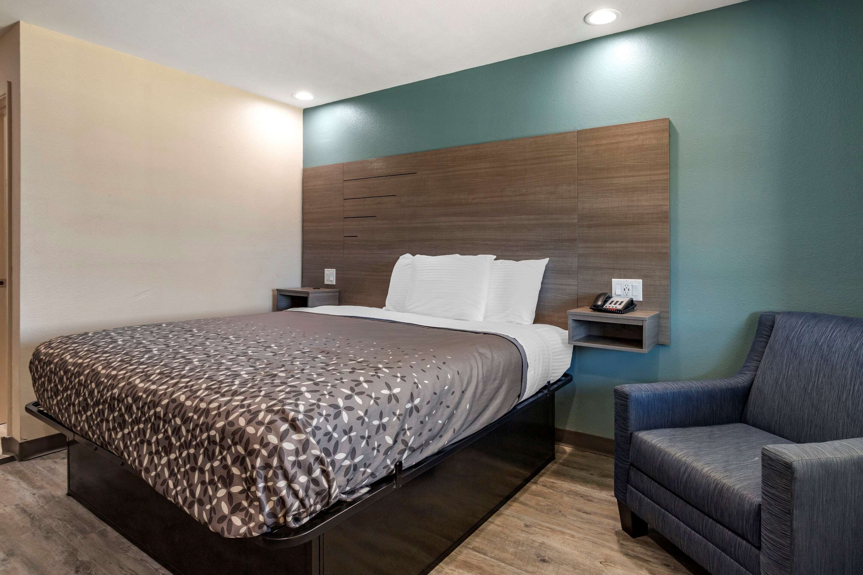 Habitación de hotel moderna con una cama grande, una silla y una mesita de noche con un teléfono.
