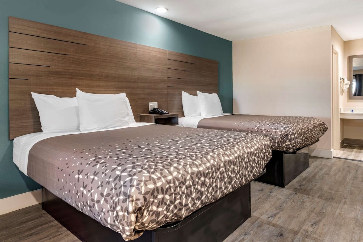 A modern hotel room with a large bed, a bedside table with a phone, and a bathroom visible through an open door.