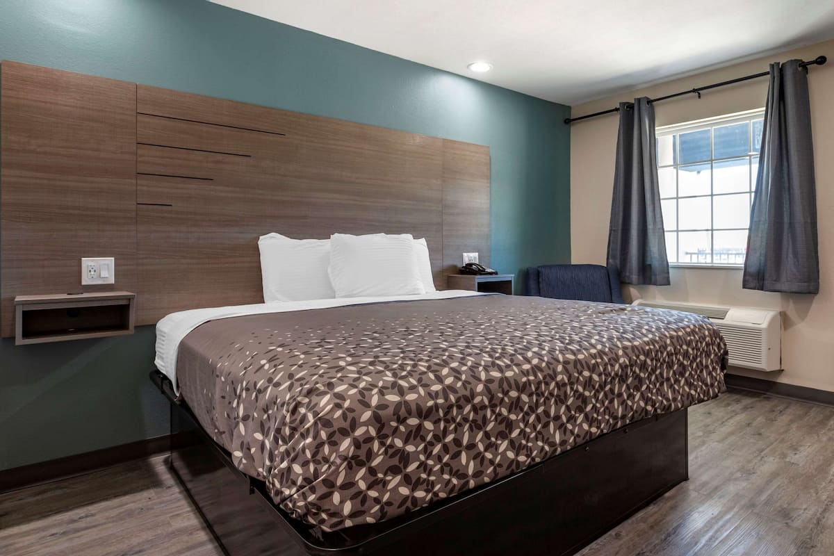 A modern hotel room with a large bed, a bedside table, a chair, and a window with curtains.
