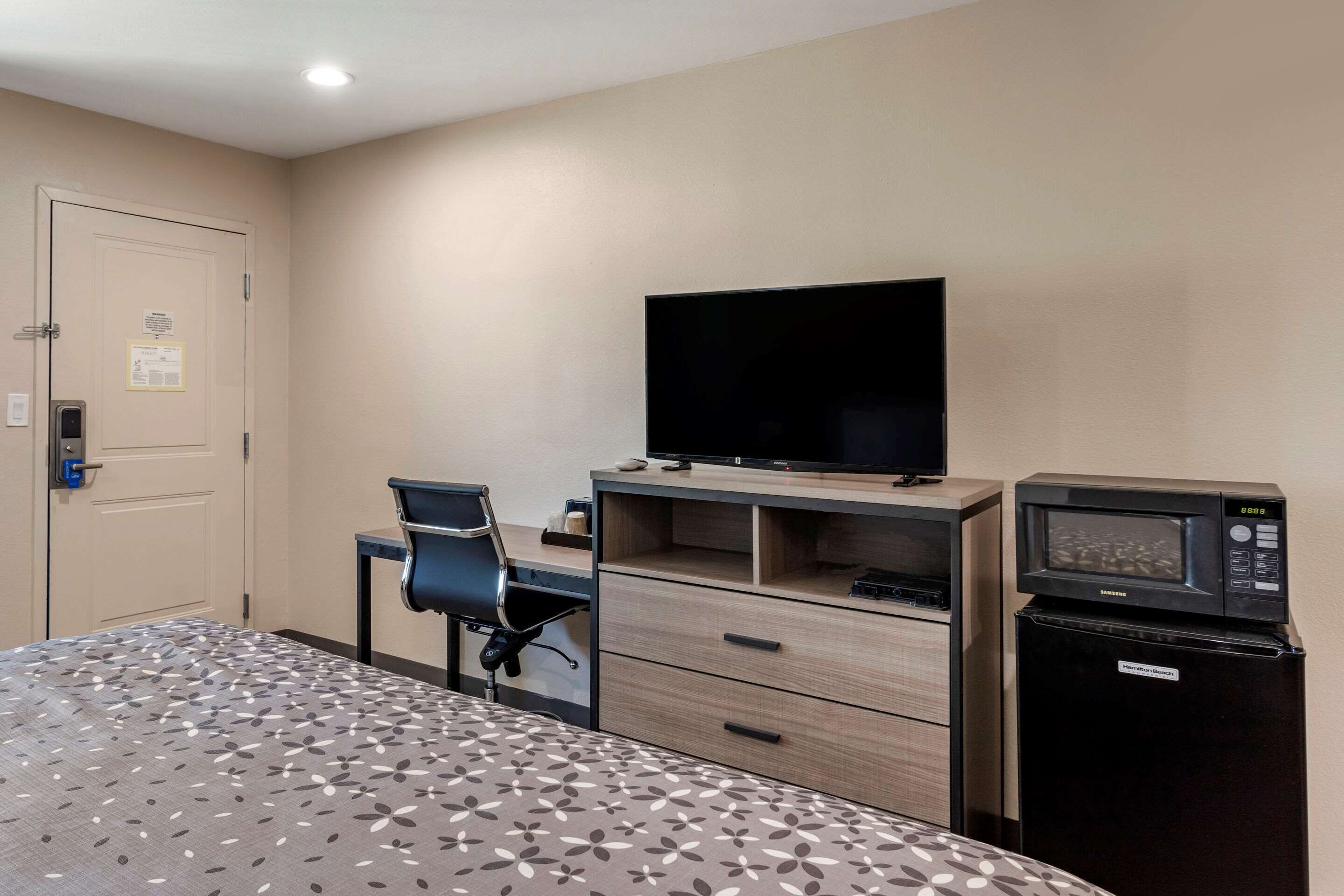 A hotel room with a bed, a desk with a computer, a television, and a microwave.