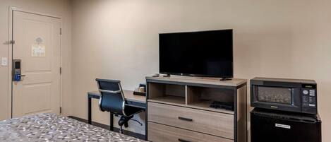 A hotel room with a bed, a desk with a computer, a television, and a microwave.