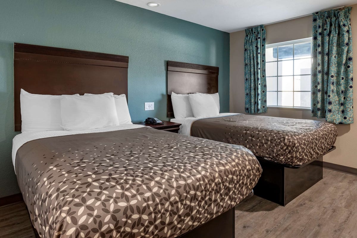 A hotel room with two beds, each with a patterned bedspread, a wooden headboard, and a nightstand with a phone.