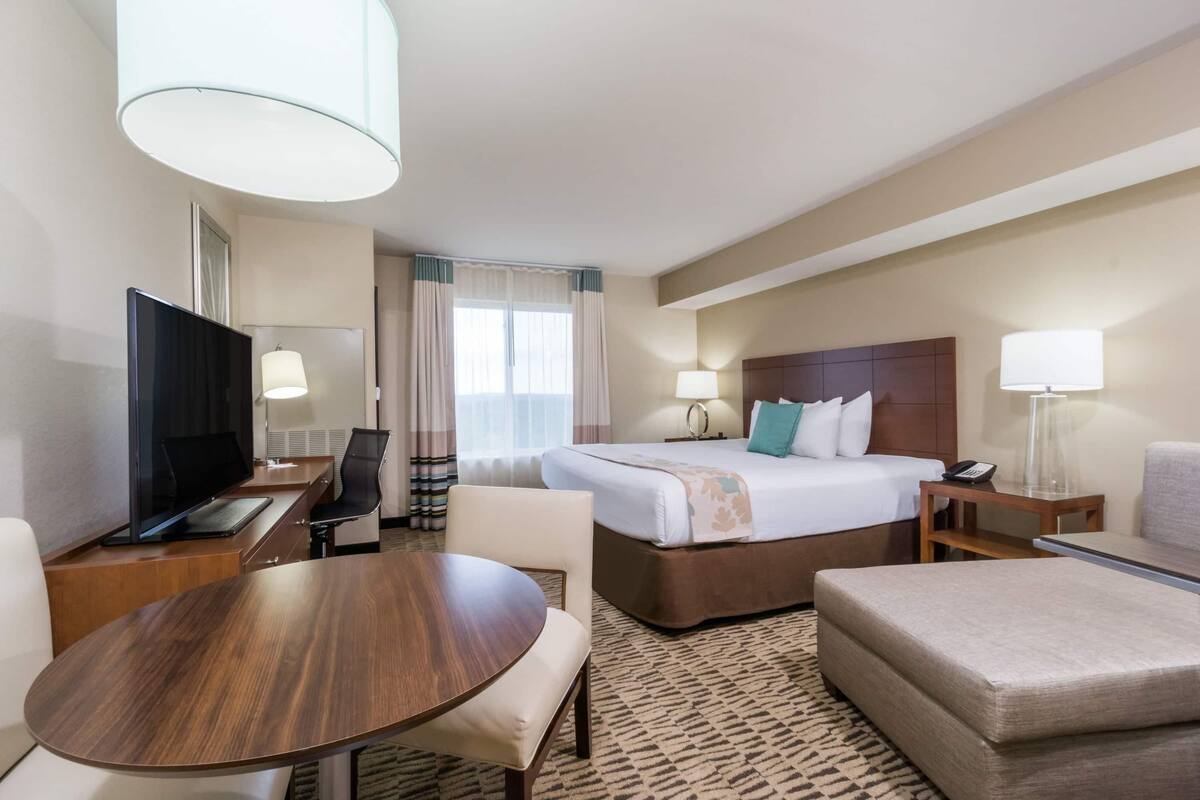 Ein Hotelzimmer mit Bett, Schreibtisch mit Fernseher, Sessel, Tisch und Lampe.