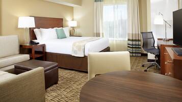 A hotel room with a bed, two bedside tables with lamps, a desk with a chair, a round table, and a television.