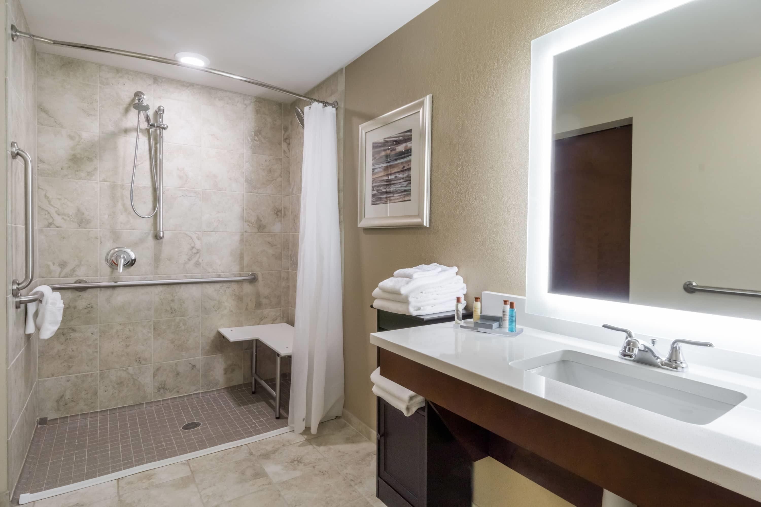 A bathroom with a shower, a sink, a mirror, and a towel rack.