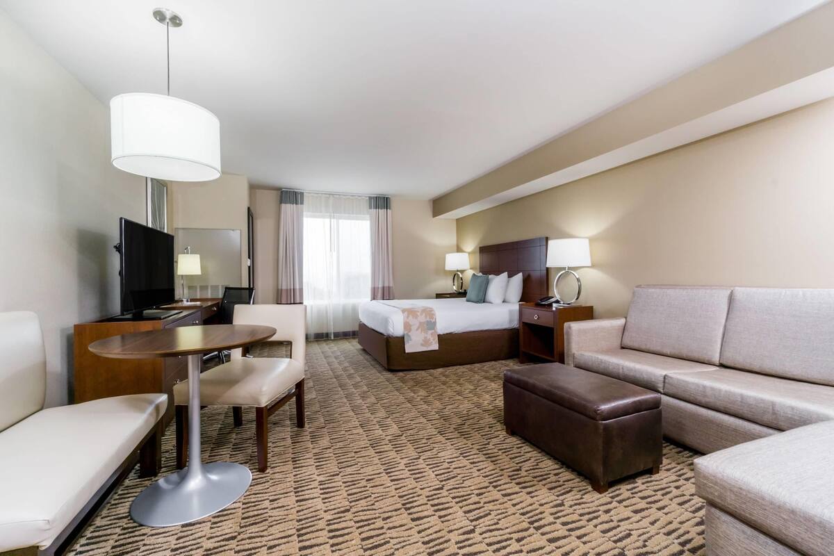 Ein Hotelzimmer mit Bett, Sofa, Schreibtisch, Stuhl, Fernseher und Lampe.