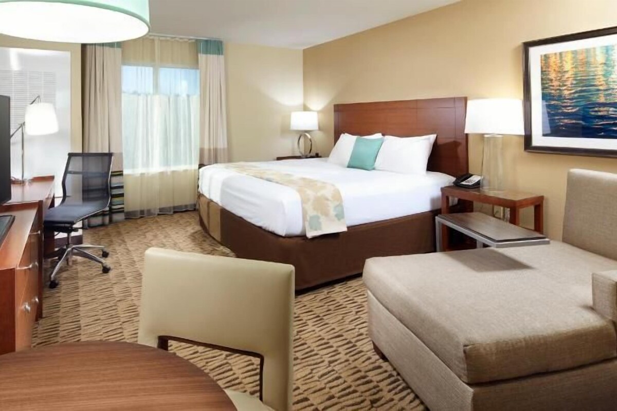 A hotel room with a bed, a desk with a TV, a chair, a sofa, and a carpeted floor.