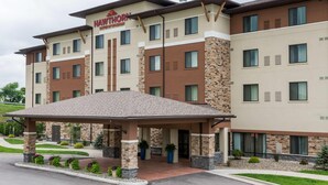 Un hotel de varios pisos con entrada cubierta, fachada de piedra y ladrillo, y un letrero que dice 'Hawthorn Suites by Wyndham'.