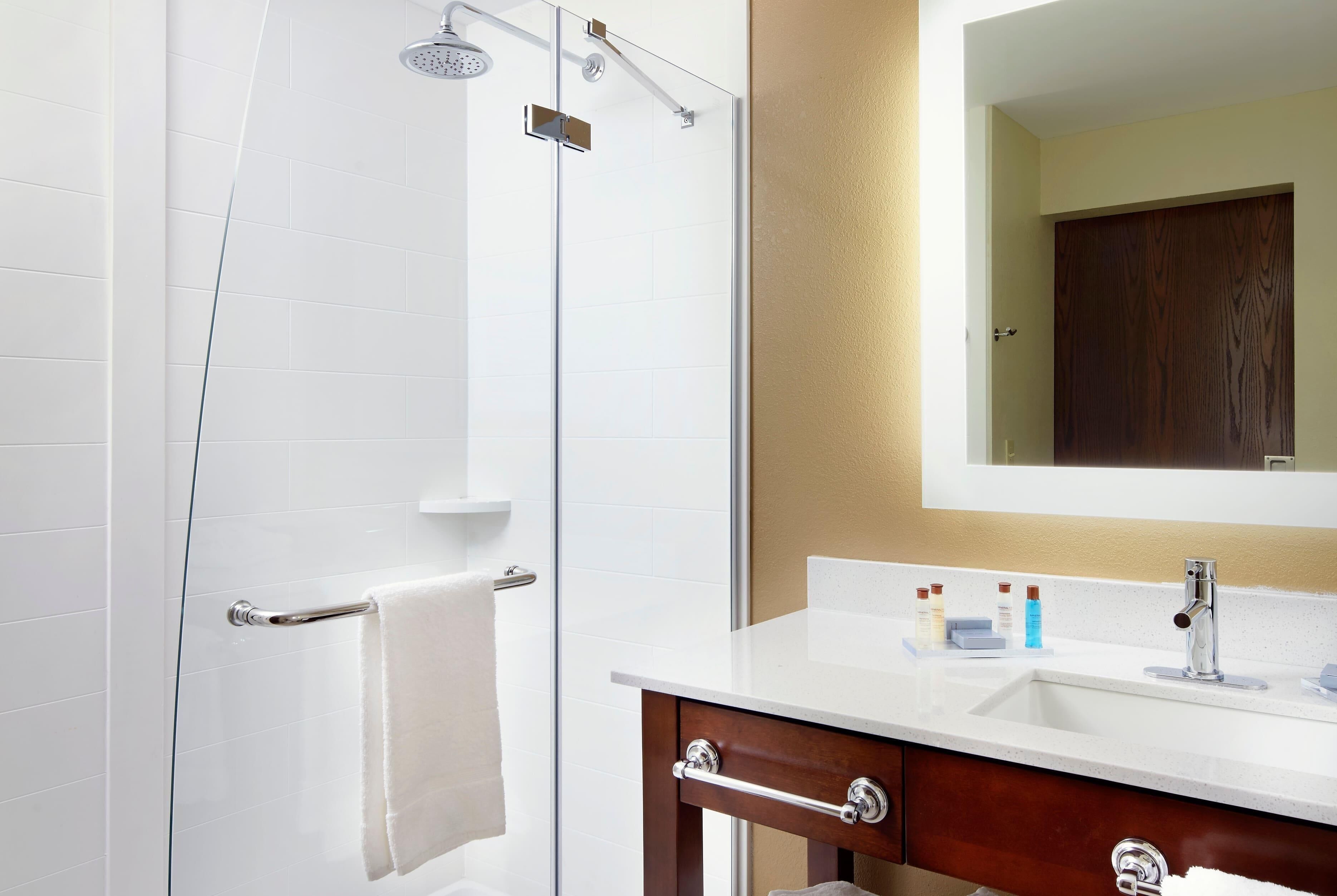A bathroom with a shower, a sink, a mirror, and a towel rack.