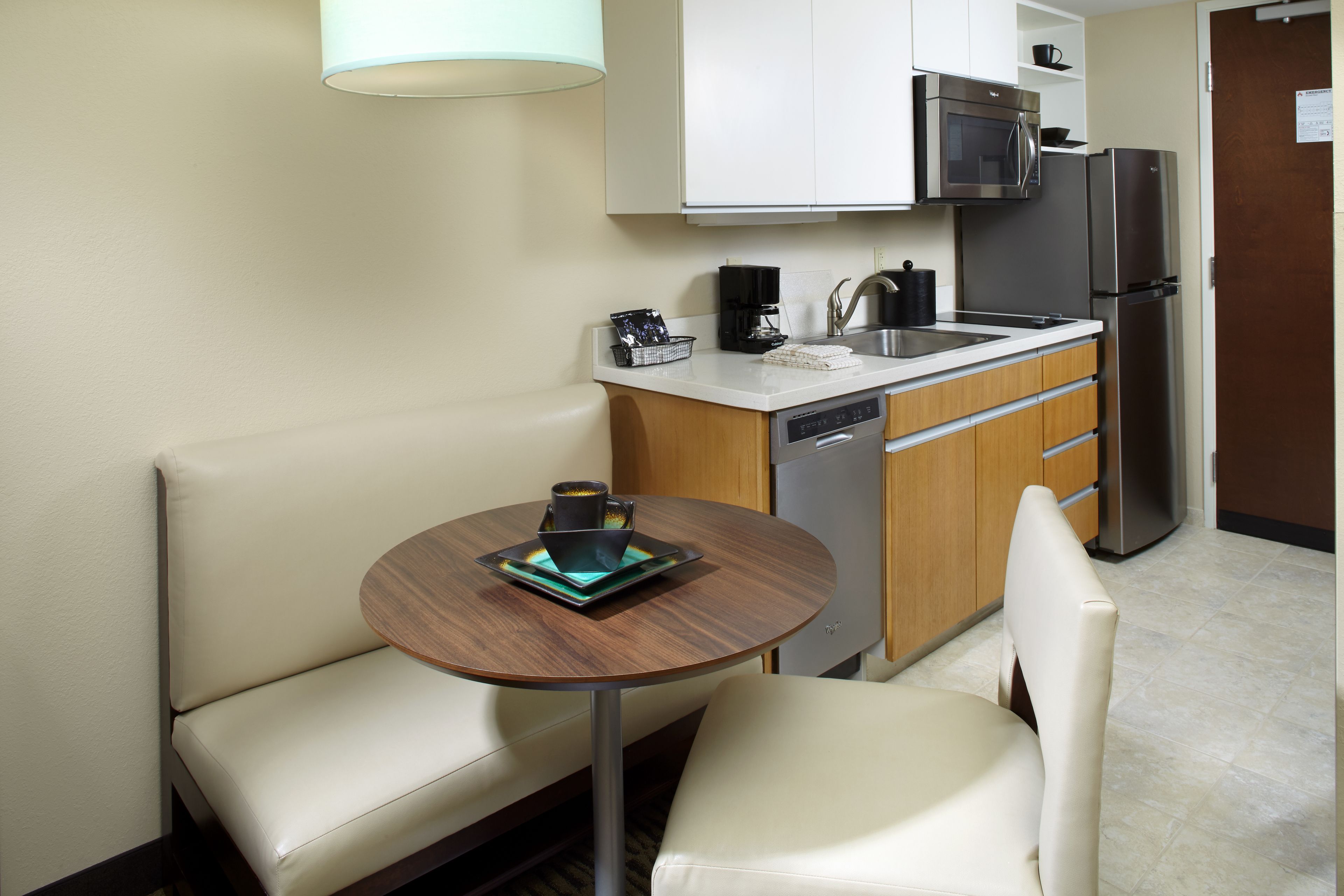 A compact kitchen with a microwave, coffee maker, and refrigerator. There is a small dining area with a table and two chairs.